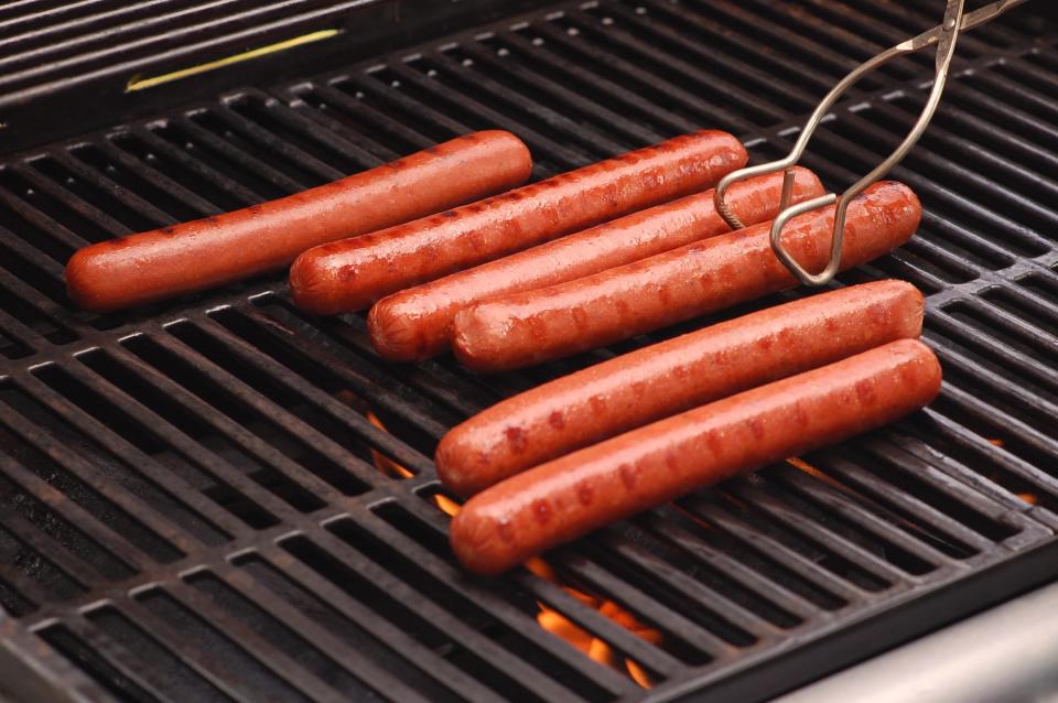 Hot dogs on grill being moved by tongs