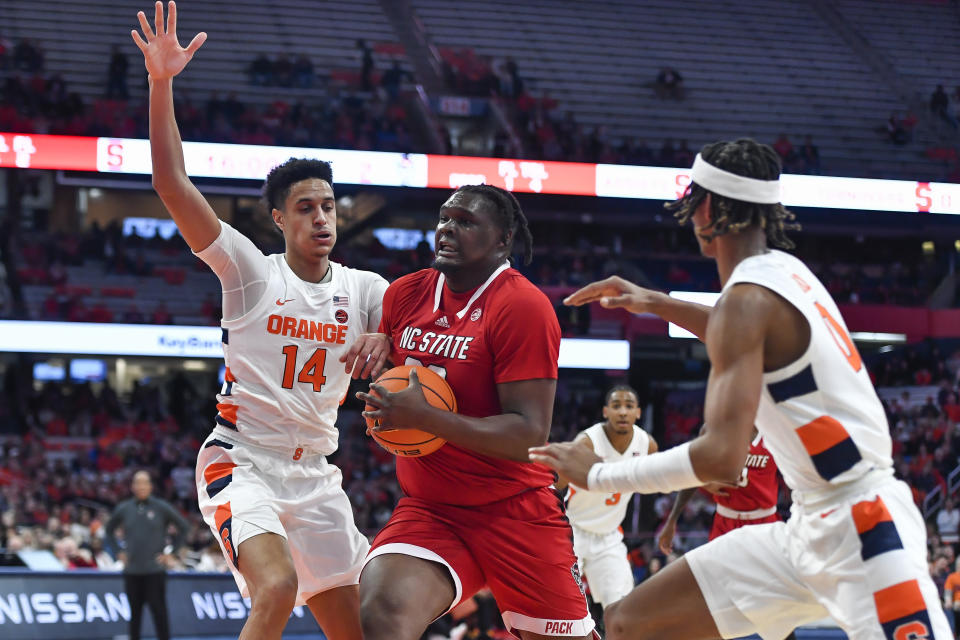 North Carolina State forward DJ Burns, Jr., center, splits the defense of Syracuse center Jesse Edwards (14) and forward Chris Bell during the first half of an NCAA college basketball game in Syracuse, N.Y., Tuesday, Feb. 14, 2023. (AP Photo/Adrian Kraus)