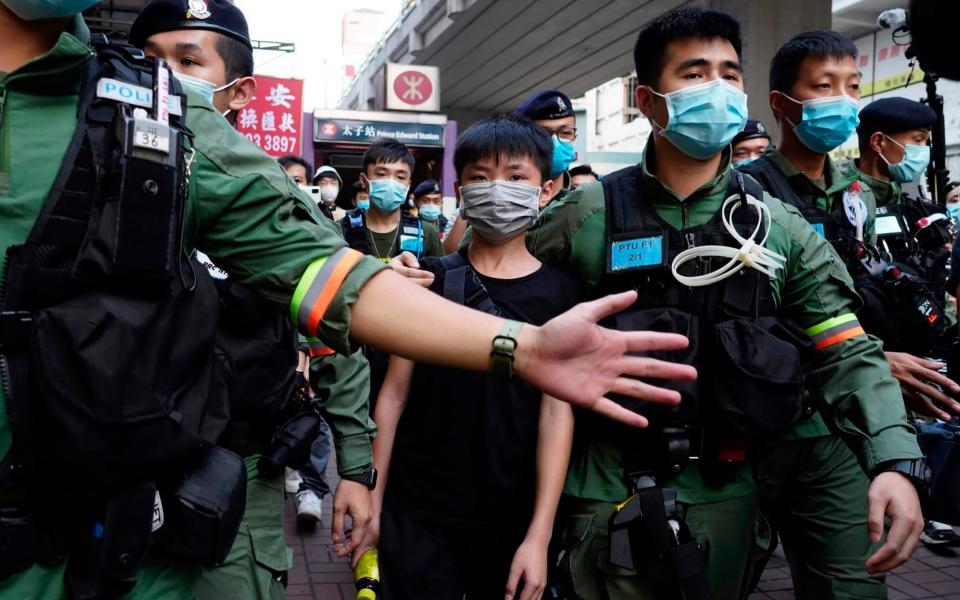 A boy is escorted away by police after trying to place flowers outside the Prince Edward subway station  - Vincent Yu/AP