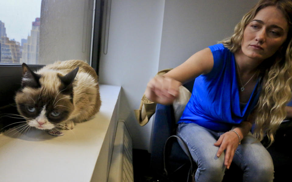 Tabatha Bundesen and her cat, Grumpy Cat,whose real name is Tardar Sauce, pose for a photograph on Friday April 4, 2014 in New York.  Bundesen says that Grumpy Cat's permanently grumpy-looking face is due to feline dwarfism.  (AP Photo/Bebeto Matthews)