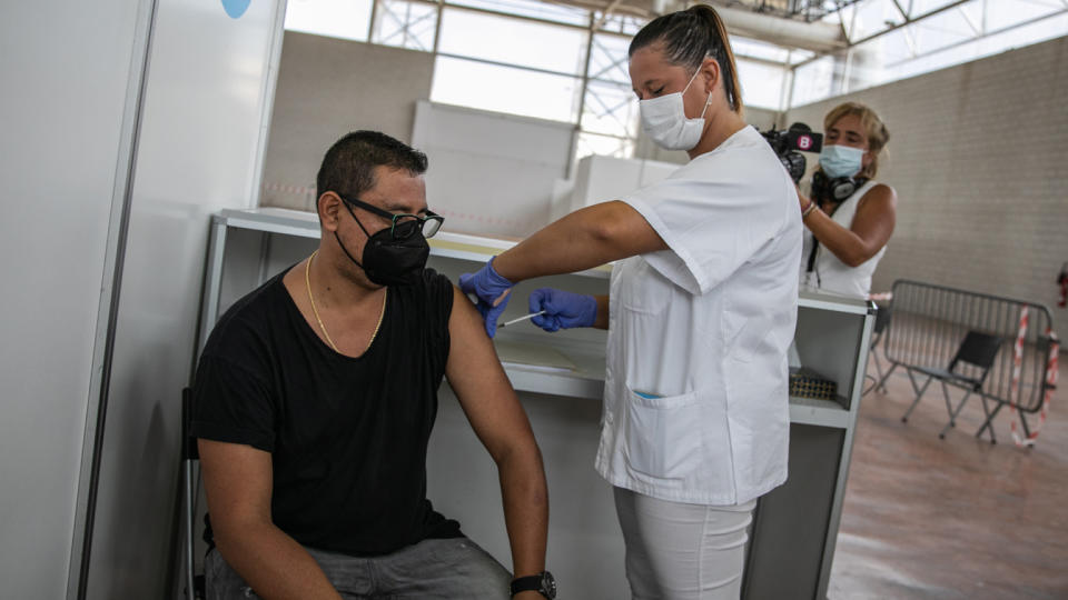 A man in a T-shirt, wearing a face mask, sits as he receives a third dose of the Pfizer COVID-19 vaccine in Ibiza, Spain. 