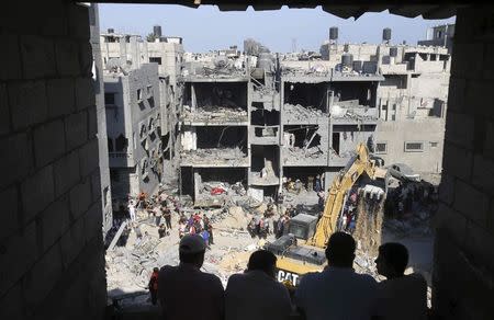 Palestinians watch as rescue workers search for victims under the rubble of a house, which witnesses said was destroyed in an Israeli air strike that killed three senior Hamas military commanders, in Rafah in the southern Gaza Strip August 21, 2014. REUTERS/Ibraheem Abu Mustafa