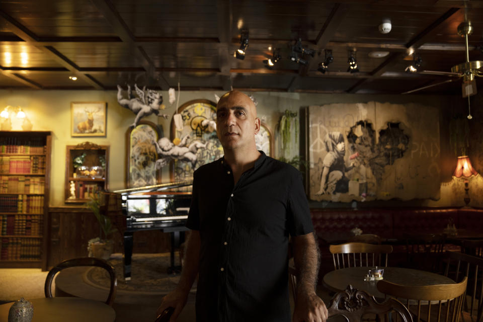 Wisam Salsaa, manager of the Walled Off Hotel, poses in the lobby with works by artist Banksy in the West Bank city of Bethlehem, Sunday, June 19, 2022. Summer travel is underway across the globe, but a full recovery from two years of coronavirus could last as long as the pandemic itself. “Tourism here," Salsaa said, "is very fragile.” (AP Photo/Maya Alleruzzo)