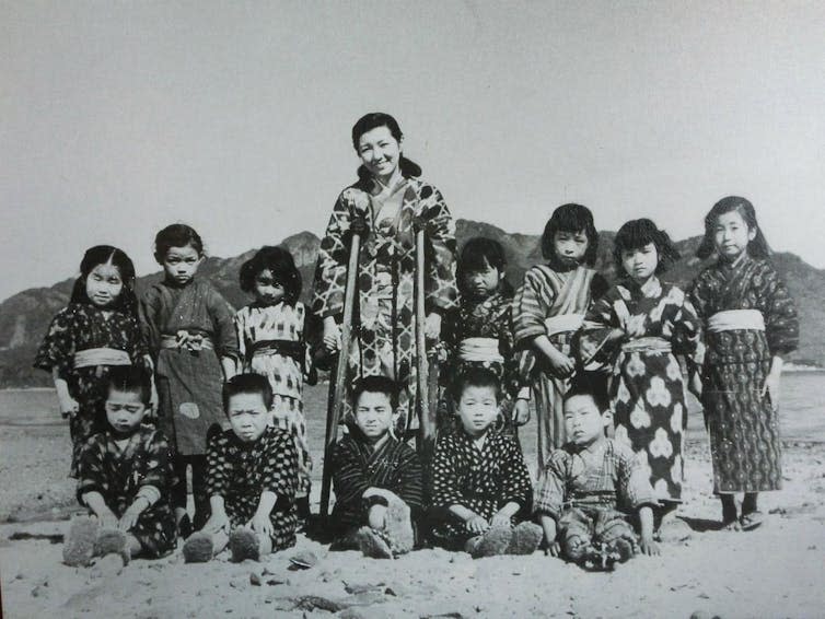 Black and white photo of a teacher surrounded by her young students.