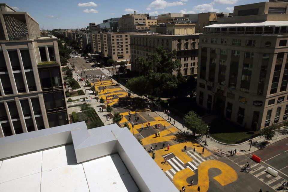 FILE - In this June 7, 2020, people walk on the words Black Lives Matter that was painted in bright yellow letters on 16th Street as demonstrators protest near the White House in Washington, over the death of George Floyd. Black Lives Matter activists are holding a virtual Black National Convention Friday, Aug. 28, to adopt a political agenda calling for slavery reparations, universal basic income, environmental justice and legislation that entirely re-imagines criminal justice reforms. (AP Photo/Maya Alleruzzo, File)