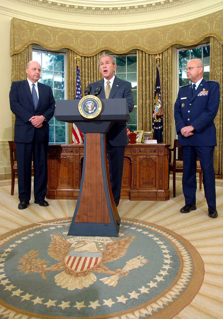 U.S. President George W. Bush (C) speaks as former director of the National Security Agency Gen. Michael Hayden (R) and Director of National Intelligence John Negroponte (L) look on during a personnel announcement May 8, 2006 in the Oval Office of the White House in Washington, DC. (Photo by Roger Wollenberg-Pool/Getty Images)