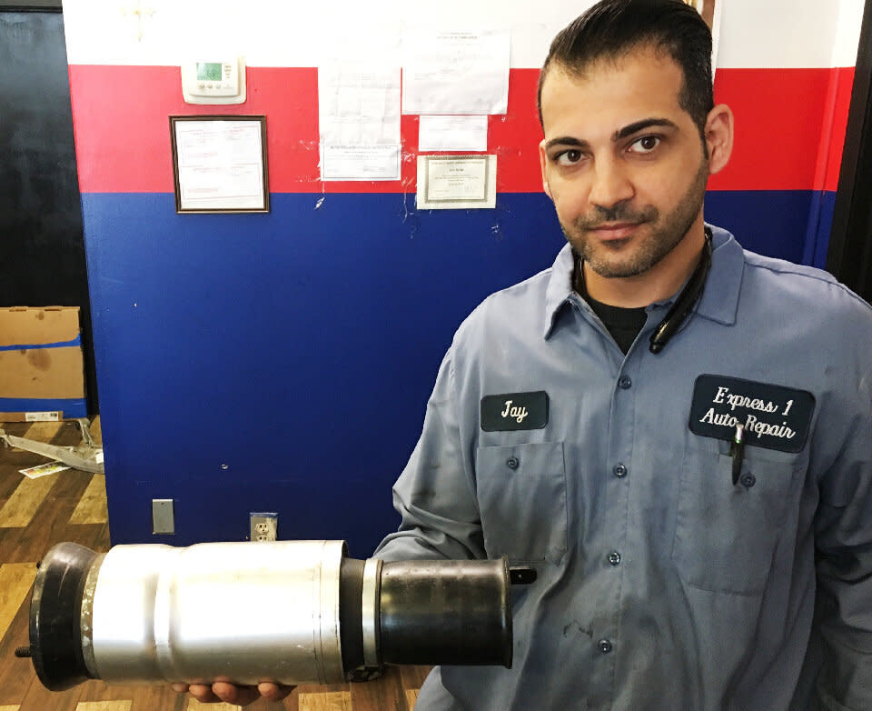 Mechanic Jay Buni says the potholes on the roads around his shop in Warren, Michigan, ruin wheels and suspensions all the time. The damaged strut he's holding came from his own car, which he no longer drives to work. (Photo: HUFFPOST/Jonathan Cohn)