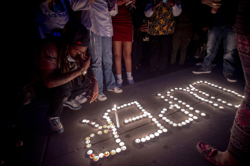 In this Sunday, May 3, 2020, photo, Maalik Mitchell, 20 of Flint, copes with the death of his father Calvin Munerlyn, kneeling next to a display of candles that spell out Munerlyn's nickname "Duper" during a vigil in Flint, Mich. A woman, her adult son and husband have been charged in the fatal shooting of Munerlyn, a security guard who refused to let her daughter enter a Family Dollar in Michigan because she wasn't wearing a face mask to protect against transmission of the coronavirus. (Jake May/The Flint Journal-MLive.com via AP)