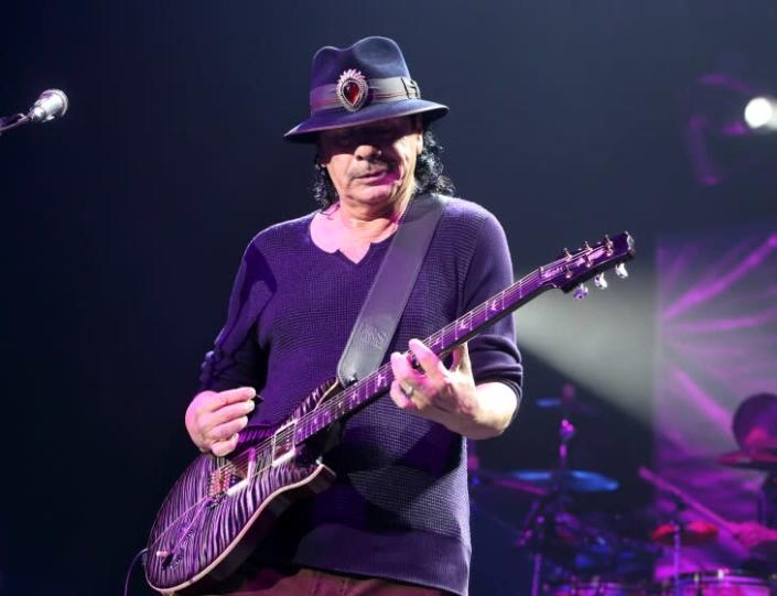 A man wearing a black hat looks down as he plays the guitar onstage