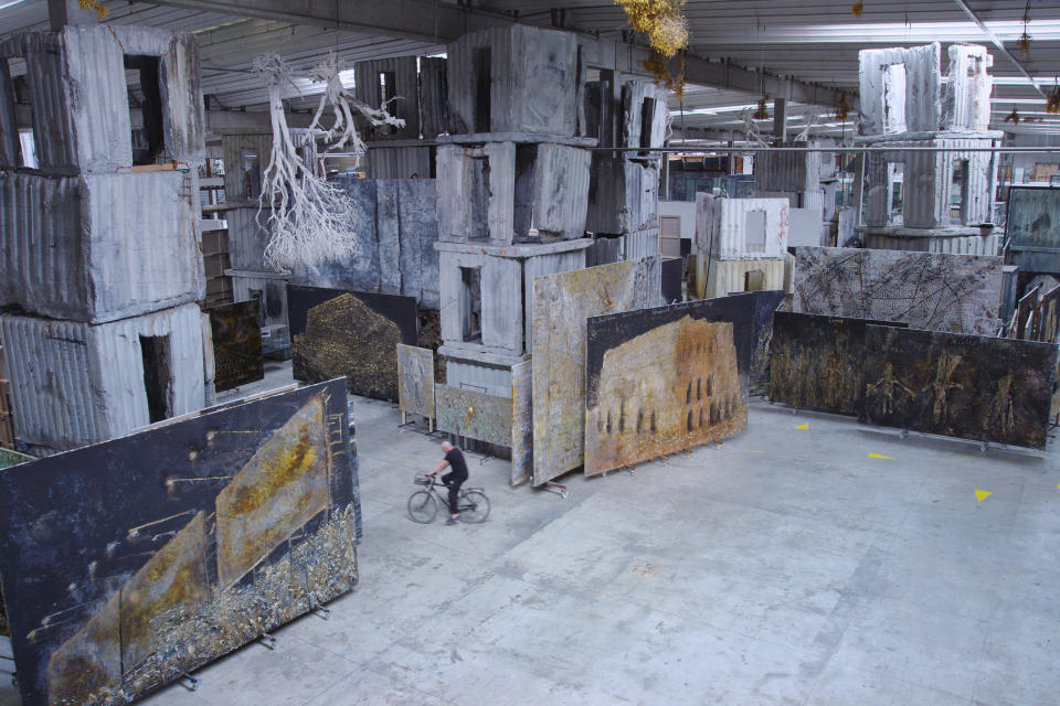 Artist Anselm Kiefer rides a bicycle in his cavernous studio space in France.