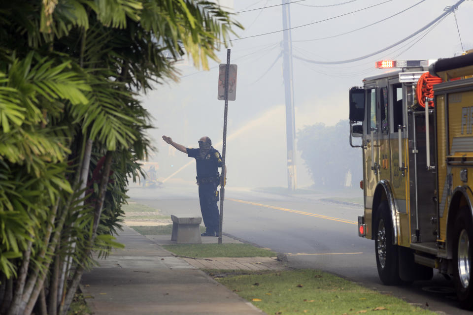 A Honolulu police officer directs traffic near the scene of multiple house fires in the Diamond Head neighborhood Sunday, Jan. 19, 2020, in Honolulu, following a shooting in which two police officers were shot. (AP Photo/Marco Garcia)