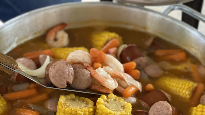 Shrimp, sausage, and corn cobs in water in pot