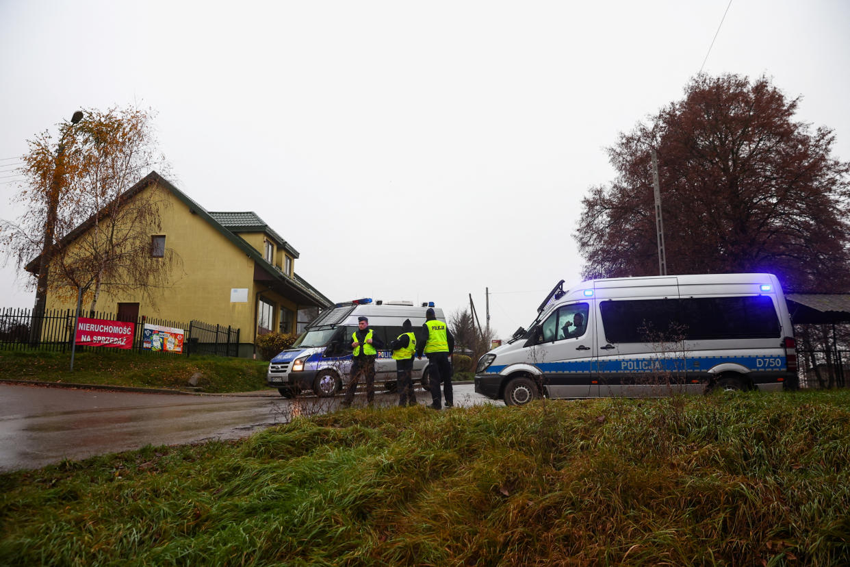 Three police officers stand in the road by two police vans, one of which appears to be blocking the road.