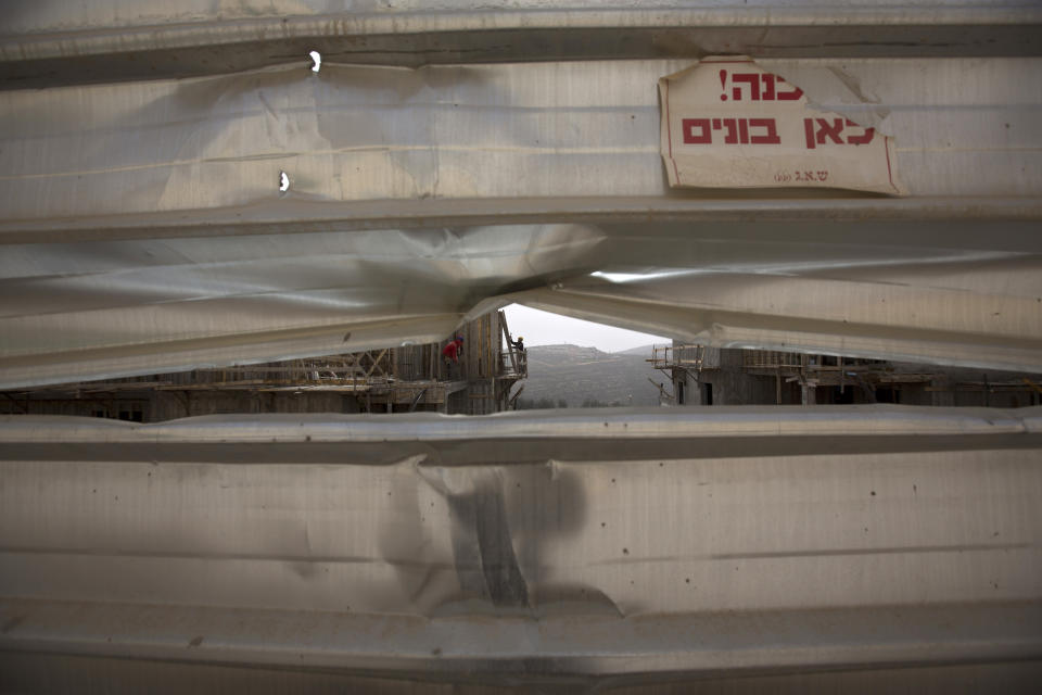 In this photo taken Monday, March 3, 2014, a worker is seen at a construction site in the Jewish settlement of Eli. Ahmed Awais has been desperate to get out of his parents' cramped home where he, his wife and three pre-school children share one room, sleeping on mattresses on the floor at night. Hebrew on sign reads:"Danger construction here." (AP Photo/Sebastian Scheiner)