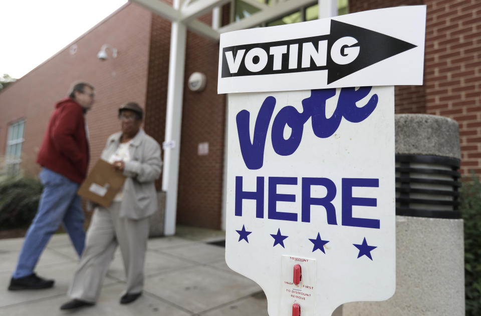 A voter arrives as a worker walks past during early voting at a polling place in Charlotte, N.C., Tuesday, Oct. 23, 2018. (AP Photo/Chuck Burton)