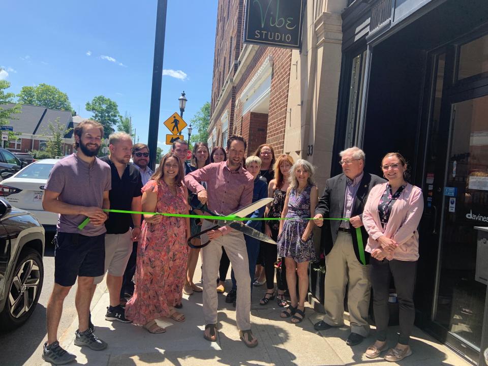 Surrounded by city officials and co-workers, Vibe Studio owner Eric DeJackome uses a pair of giant scissors to cut the ribbon in front of his studio at 33 Pleasant St., Gardner, on Monday, June 6.  From left, Hudson Carlson, Ryan Akin, state Rep. Jonathan Zlotnik, Natasha Pesce, Mayor Michael Nicholson, City Council President Elizabeth Kazinskas, Economic Development Coordinator Jessica DeRoy, DeJackome, Tatiana Selesky, Square 2 Gardner President Patti Bergstrom, Michelle Swan, Denise Cerrati, Greater Gardner Chamber of Commerce Director Michael Gerry, and Greater Gardner Chamber of Commerce Director of Marketing and Communication Rebecca Marois.