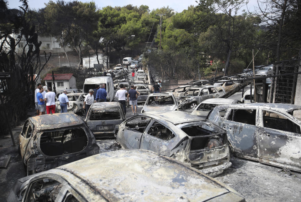FILE - People stand amid the charred remains of burned-out cars in Mati east of Athens, Greece, Tuesday, July 24, 2018. A court on Monday, April 29, 2024, has convicted five former Fire Service and disaster response officials over a 2018 wildfire outside Athens that killed more than 100 people. (AP Photo/Thanassis Stavrakis, File)