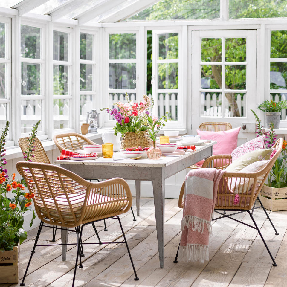 White conservatory with wooden floor and dining table surrounded by rattan chairs