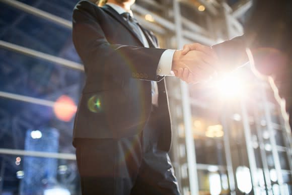 Two people in suits shaking hands in front of a building.