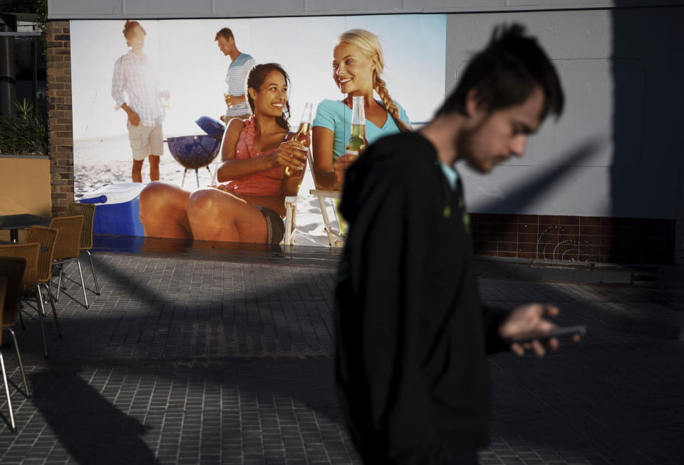 Sam Ware, 22, walks past a billboard while out on a morning walk from the hostel where he is staying at The Entrance, Central Coast, Australia, Thursday, July 25, 2019. Sam lost friends and family and most of his belongings through his addiction. His phones, laptop and clothes were left behind or stolen while overdosing on trains, in shopping centers, in a library. (AP Photo/David Goldman)