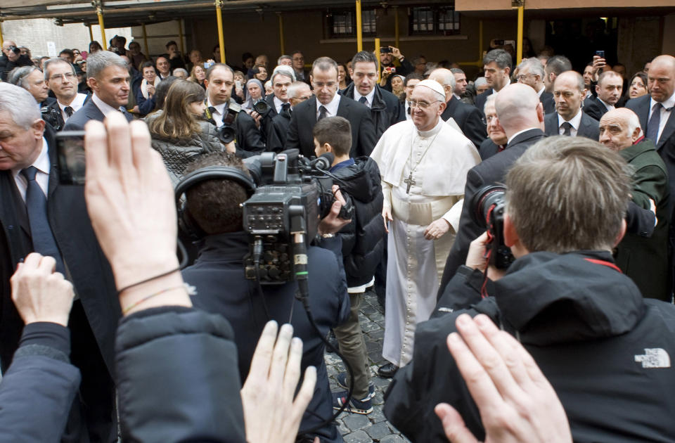 Pope Francis greets faithful at the Vatican, Sunday, March 17, 2013. Pope Francis began his first Sunday as pontiff by making an impromptu appearance to the public from a side gate of the Vatican, startling passersby and prompting cheers, then kept up his simple, spontaneous style by delivering a brief, off-the-cuff homily at the Vatican's tiny parish church. Dressed only in white cassock, Francis waved to the crowd in the street outside St. Anna's Gate and before entering the church, which serves Vatican City State's hundreds of residents, he shook hands of the parishioners and kissed babies. (AP Photo/Antonello Nusca)