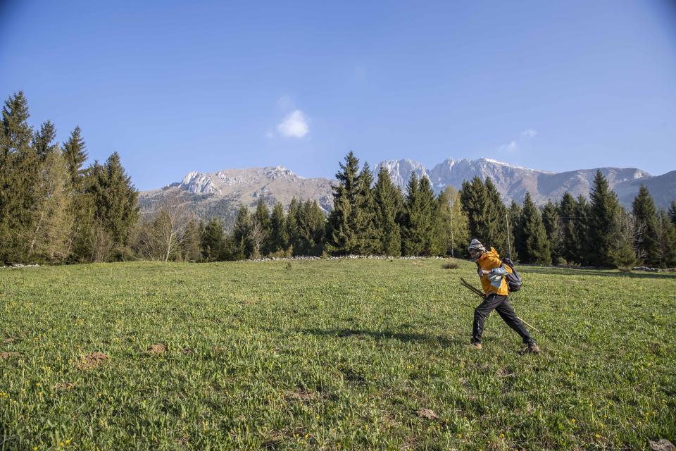 In this image taken on Thursday, April 23, 2020, alpine guide Ernesto Cocchetti, 57, walks on a slope in Castione Della Presolana, with Mt. Presolana in the background, near Bergamo, northern Italy. Cocchetti normally works the in summer, taking clients as young as 8 on hiking tours, and older clients up to the peaks of "The Queen of the Orobie", but he also takes care of the maintenance of the Italian Alpine Club mountain paths. Cocchetti predicts a return to "living with nature's rhythms" once government restrictions to prevent the spread of COVID-19 will be eased. (AP Photo/Luca Bruno)