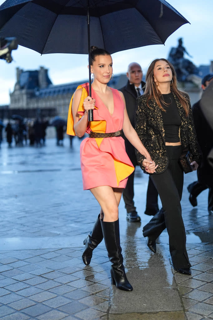 Milly Bobby Brown holding an umbrella and walking with others