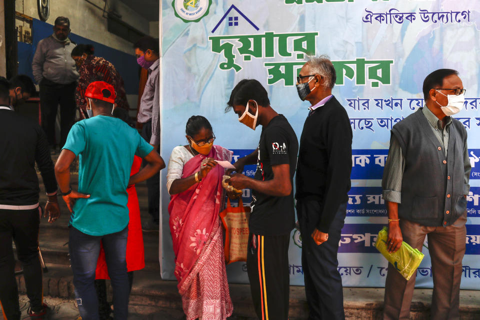 Indians wearing face masks as a precautionary measure against the coronavirus stand in a queue to apply for a health card initiated by West Bengal state government in Kolkata, India, Saturday, Jan. 2, 2021. (AP Photo/Bikas Das)