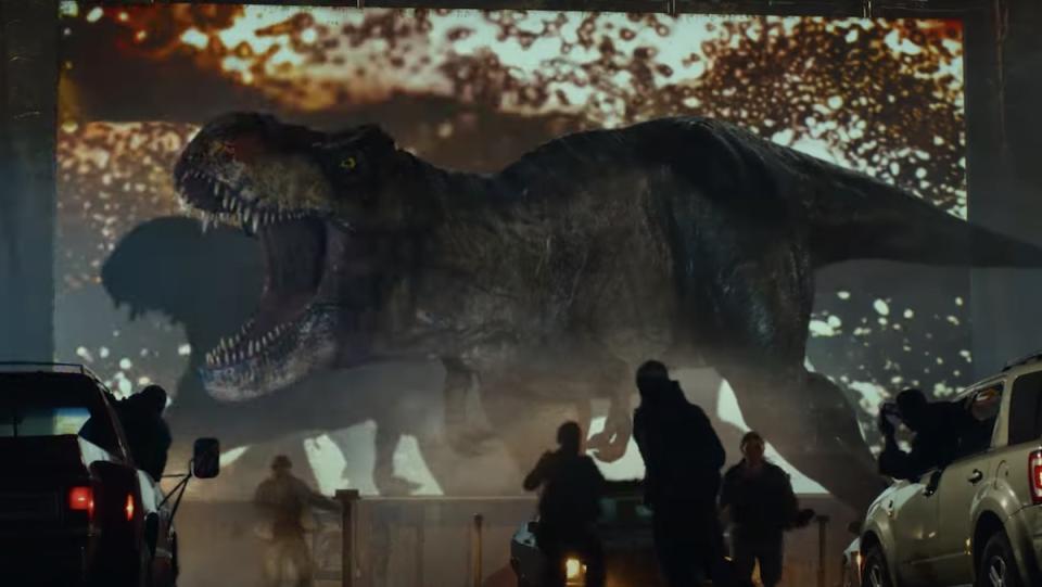 A T.rex roars in front of a drive-in theater screen as people flee in a prologue short for Jurassic World: Dominion