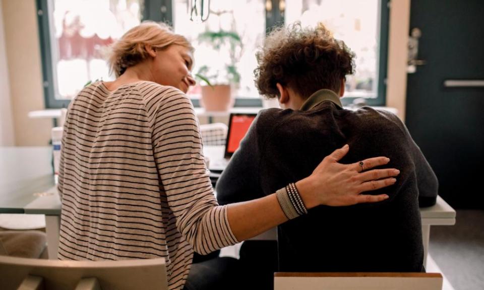 Mother sitting by teenage son studying at home