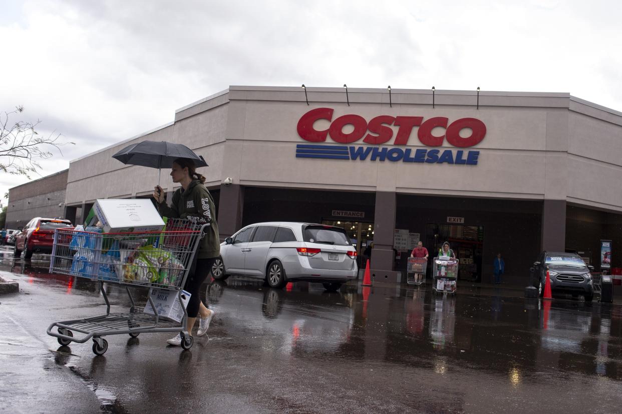 People walk with groceries in the rain outside of a Costco Wholesale store at 44th and Oak streets on March 13, 2020, in Phoenix.