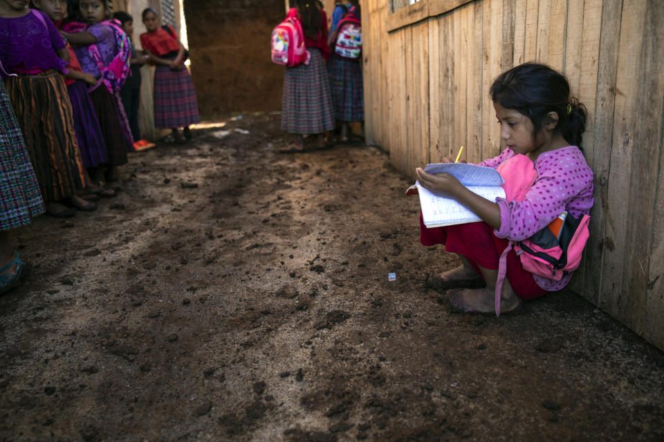 A student writes in her notebook as she crouches against a wall on the muddied floor of a shack serving as a schoolhouse which was inundated by heavy rains the night before, in the makeshift settlement Nuevo Queja, Guatemala, Tuesday, July 6, 2021. UNICEF donated a new school to the community, but it has been closed for five months because no one could find the key to open it. (AP Photo/Rodrigo Abd)