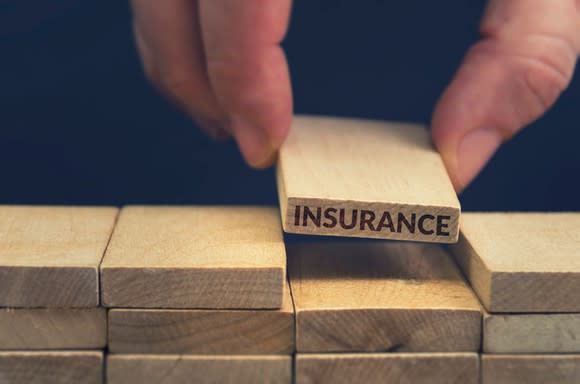 Neatly stacked wood blocks with one block labeled insurance being lifted by two fingers.