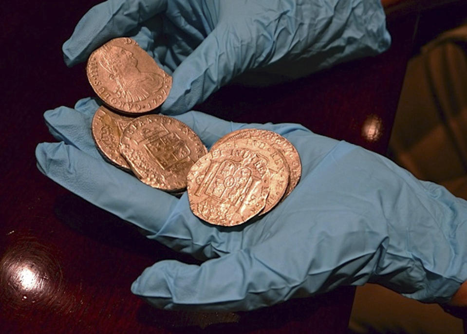 In this undated photo made available by the Spain's Culture Ministry, a member of the Ministry technical crew displays some of the 594,000 coins and other artifacts found in the Nuestra Senora de las Mercedes, a Spanish galleon sunk by British warships in the Atlantic while sailing back from South America in 1804, in a warehouse in Tampa, Fla. A 17-ton trove of silver coins recovered from the Spanish galleon was set to be flown Friday Feb. 24, 2012 from the United States to Spain, concluding a nearly five-year legal struggle with Odyssey Marine Exploration, the Florida deep-sea explorers who found and recovered it. (AP Photo/Spain's Culture Ministry, HO)