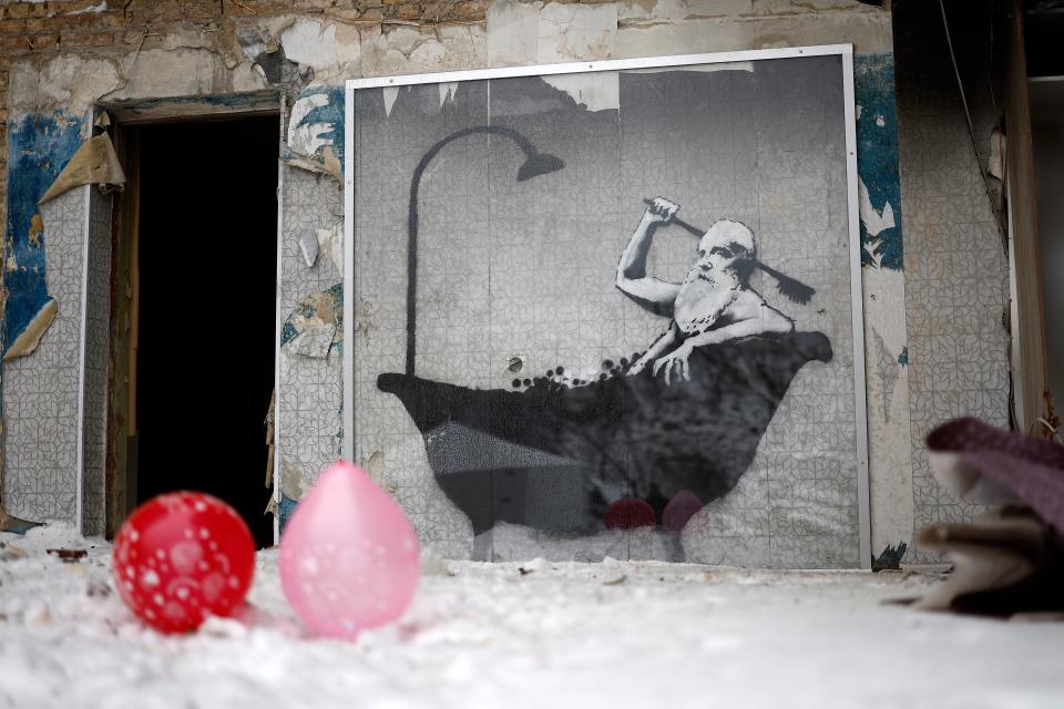 Members of public queue for food beside a picture  by graffiti artist Banksy on a the wall of a destroyed building in Horenka, Ukraine (Getty Images)