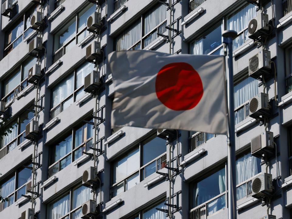 A Japanese flag blowing in the wind with a large apartment building in the background.