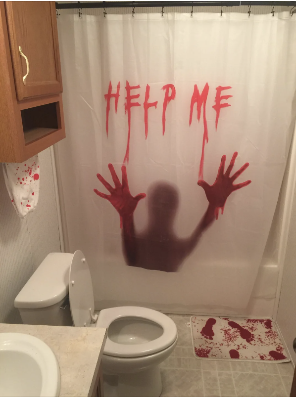 A bathroom with a shower curtain featuring a shadowy figure and the words "HELP ME" in bloody letters, along with a towel and rug both splattered with red stains