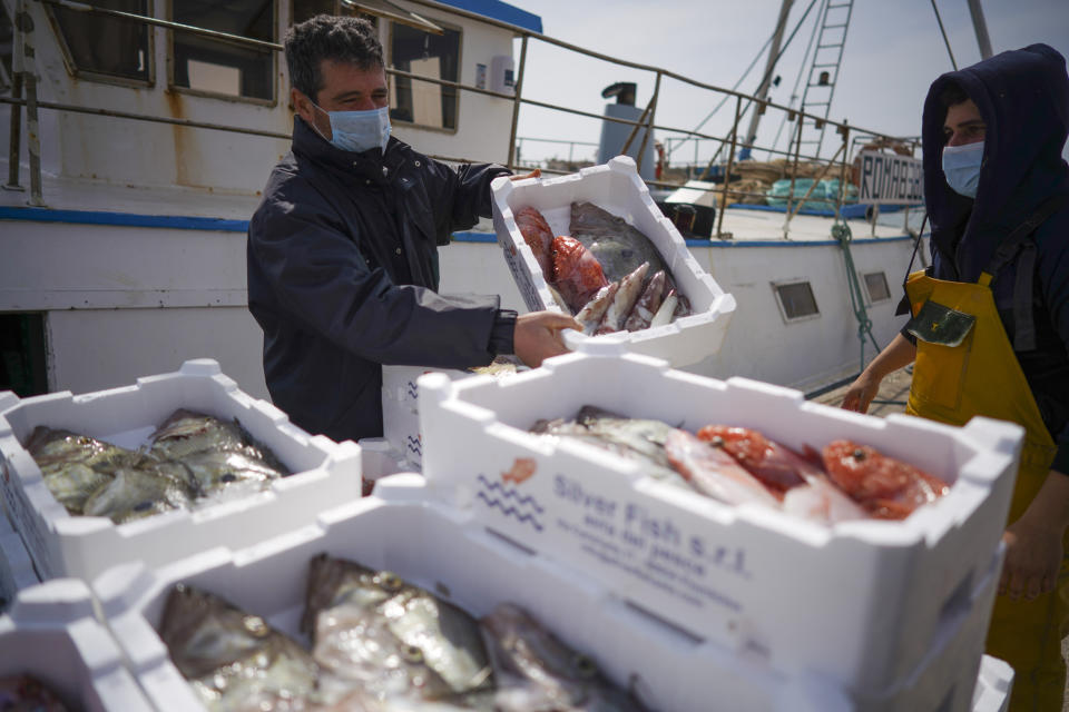 Fishermen, wearing protective masks, unload a boat at Fiumicino fishing port, in the outskirts of Rome Monday, March 30, 2020. Italy’s fishermen still go out to sea at night, but not as frequently in recent weeks since demand is down amid the country's devastating coronavirus outbreak. On Sundays, or any sunny day throughout the year, you can find several people strolling along, but since the Italian government ordered a nationwide lockdown and shut restaurants and cafés to stop the spread of Covid-19, the area is deserted, and apart from the water rippling against the quay, it is silent. (AP Photo/Andrew Medichini)