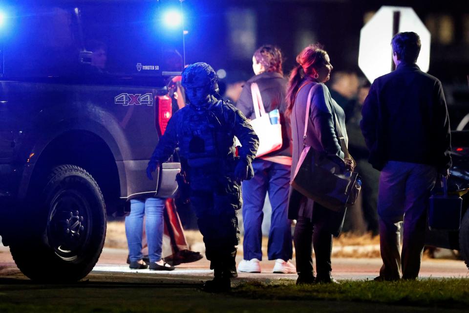 A police officer in tactical gear walks past employees waiting to access their cars in the parking lot of New Hampshire Hospital, Friday, Nov. 17, 2023. A shooter killed one person Friday in the psychiatric hospital lobby and then was fatally shot by a state trooper, officials said.