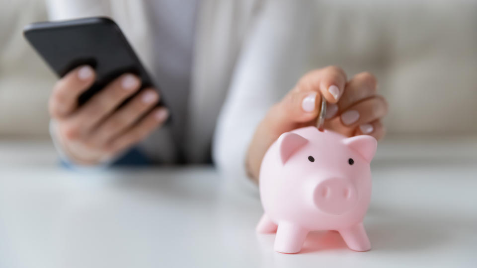 Crop close up of woman put coin in piggy bank save money for future, use financial app on cellphone, female or housewife manage household finances or expenditures, account investment on smartphone