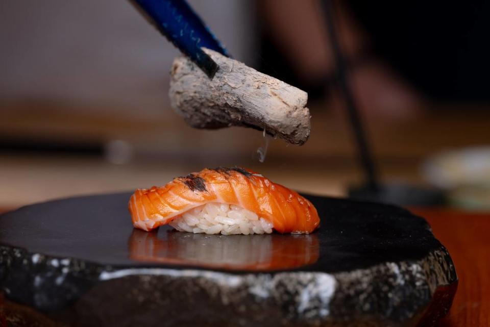 A piece of salmon nigiri is lightly torched with Binchotan (Japanese charcoal) at Omakase by Kazu.