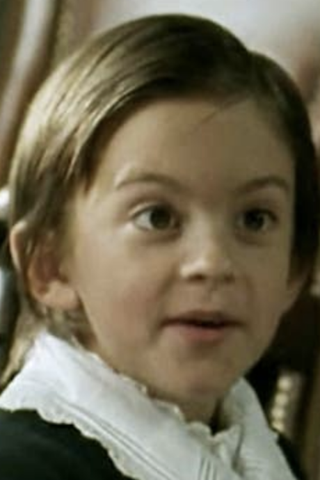 A young Jonathan Bailey in a historical costume, featuring a white ruffled collar, stares slightly off-camera. The background includes a blurred chair