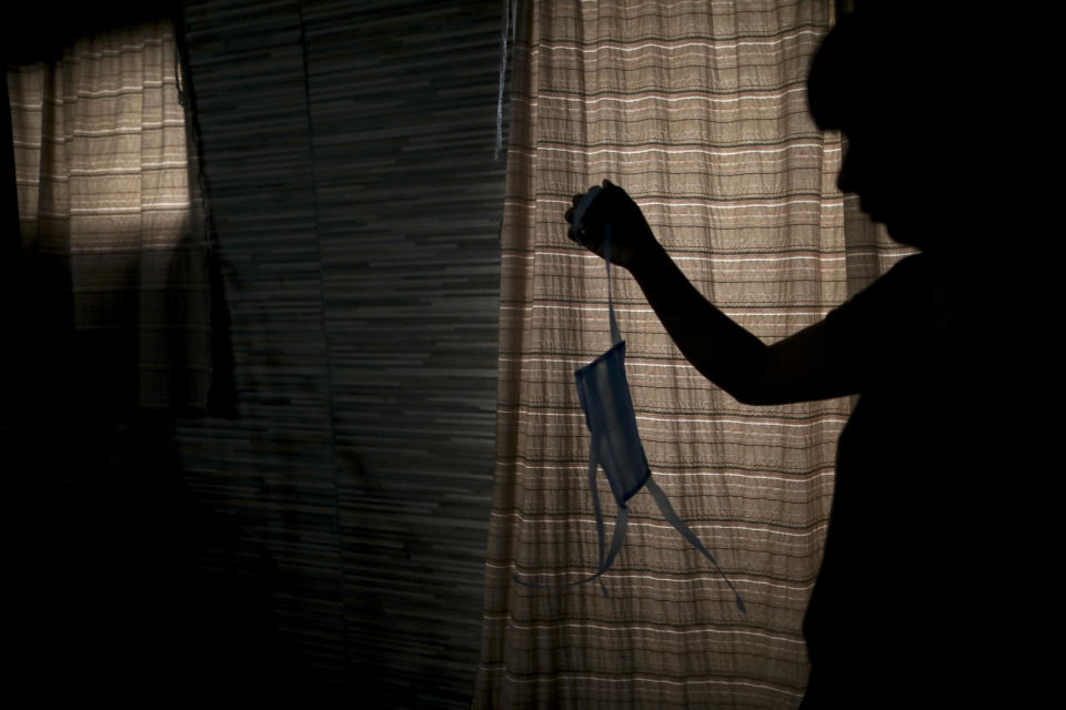 CORRECTS TO REMOVE THIRD SENTENCE STATING THEY PROVIDE FREE MASKS TO NEEDY AS WELL - Joana Maciel holds up a protective face mask that she made, as she stands inside her home on the outskirts of Buenos Aires, Argentina, Wednesday, March 25, 2020. Maciel together with other women who volunteer at a nearby soup kitchen, make the face masks to use as a precaution against the spread of the new coronavirus. (AP Photo/Natacha Pisarenko)