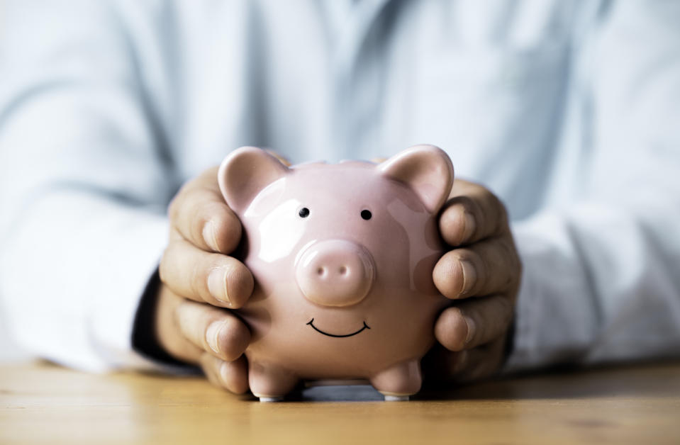 A person in a light shirt holds a small pink piggy bank with a smiling face. The image is related to financial savings and money management