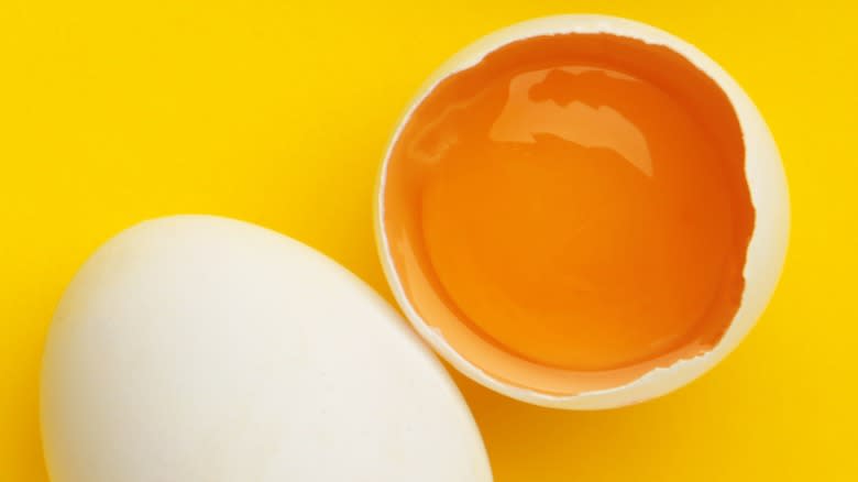 Close-up of an orange egg yolk in the shell next to a whole egg on a yellow background