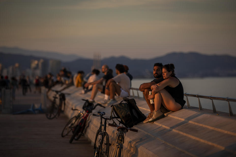 People sit on a seafront promenade during a sunset in Barcelona, Spain, Sunday, May 3, 2020. Spaniards are enjoying their second day of outdoor exercise while preparing further loosening of its lockdown measures as the country gains hold on its coronavirus outbreak. (AP Photo/Emilio Morenatti)