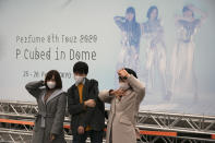 Fans wearing masks pose for photos before the start of a concert by Japanese girl group Perfume outside Tokyo Dome in Tokyo, Tuesday, Feb. 25, 2020. Japan's Prime Minister Shinzo Abe said Tuesday that new measures like companies letting their employees work from home and hospitals expanding their capacity to treat many patients will determine if Japan could control its coronavirus outbreak. (AP Photo/Jae C. Hong)