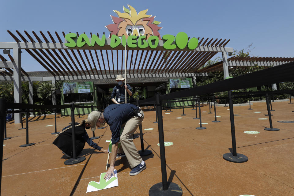 Devon Prince, front, puts down a sticker to guide visitors at the San Diego Zoo once it reopens, as Emmanuel Lopez, behind and Ariel Hayes look on, Thursday, June 11, 2020, in San Diego. California's tourism industry is gearing back up with the state giving counties the green light to allow hotels, zoos, aquariums, wine tasting rooms and museums to reopen Friday. (AP Photo/Gregory Bull)