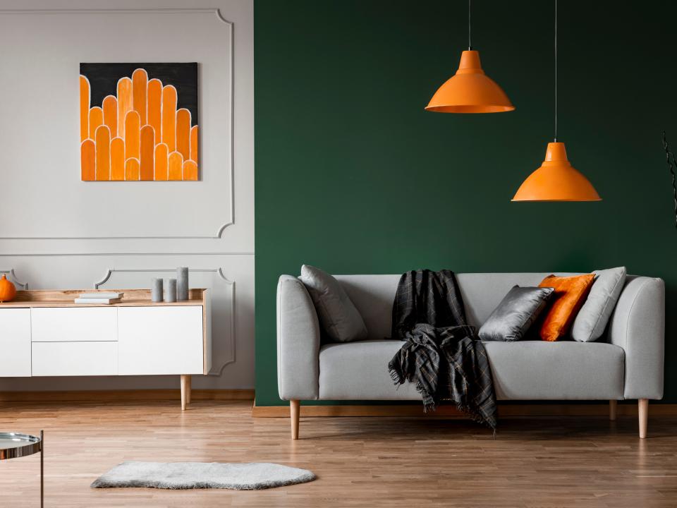 orange pops of color in a living room with a green accent wall and a gray moulding paneled wall