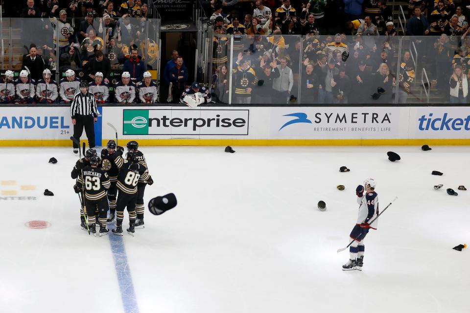 Hats fly onto the ice as Boston Bruins players congratulate teammate Brad Marchand (63) for scoring his third goal for a hat trick as Columbus Blue Jackets defenseman Erik Gudbranson (44) looks on during the third period of an NHL hockey game, Sunday, Dec. 3, 2023, in Boston. (AP Photo/Mary Schwalm)